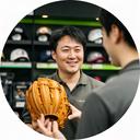 野球用品店の店長がグラブを手に店内で説明する様子